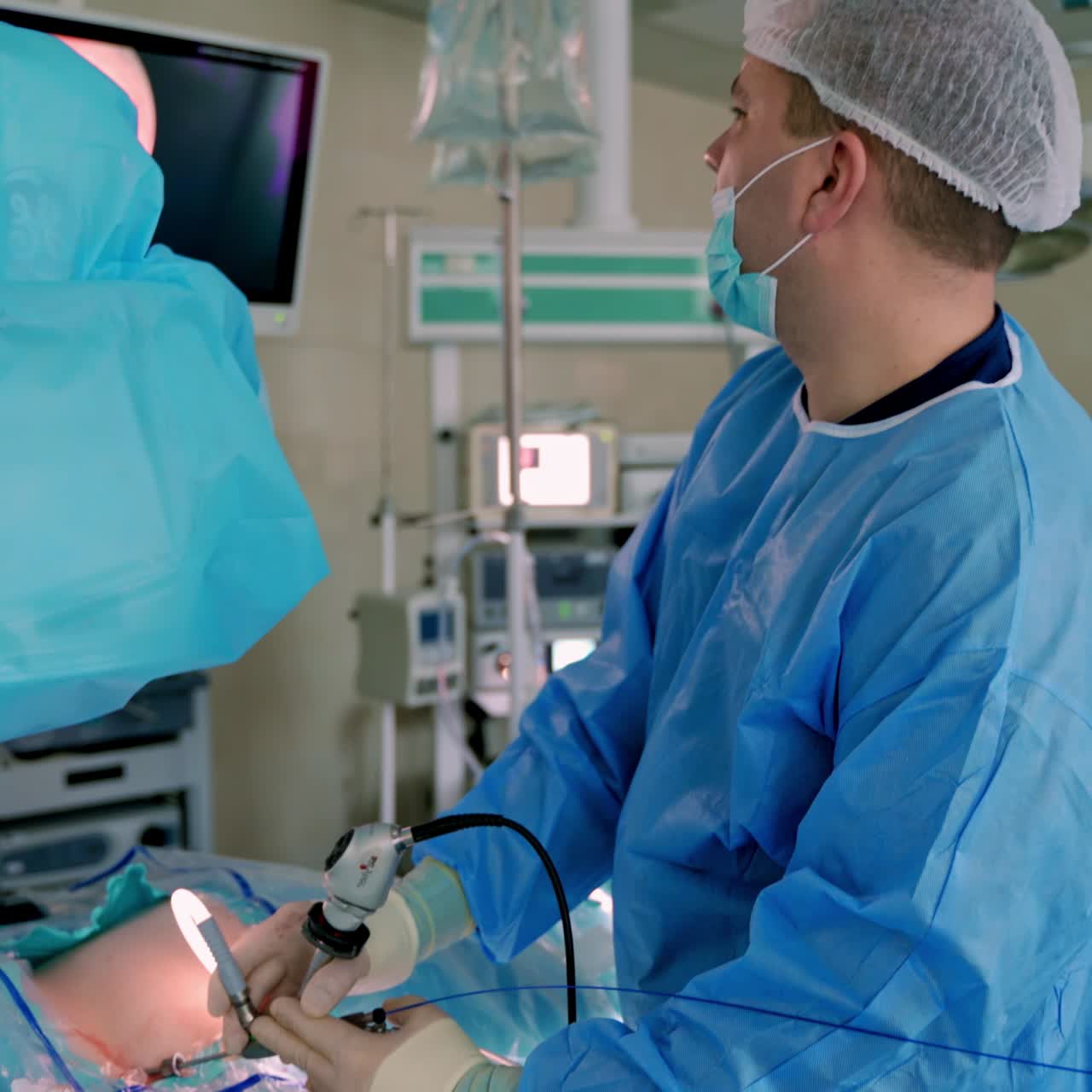 Surgeon doing operation on patient. Professional doctor in medical uniform perform a surgery to a patient and controls the process on medical monitor in hospital.