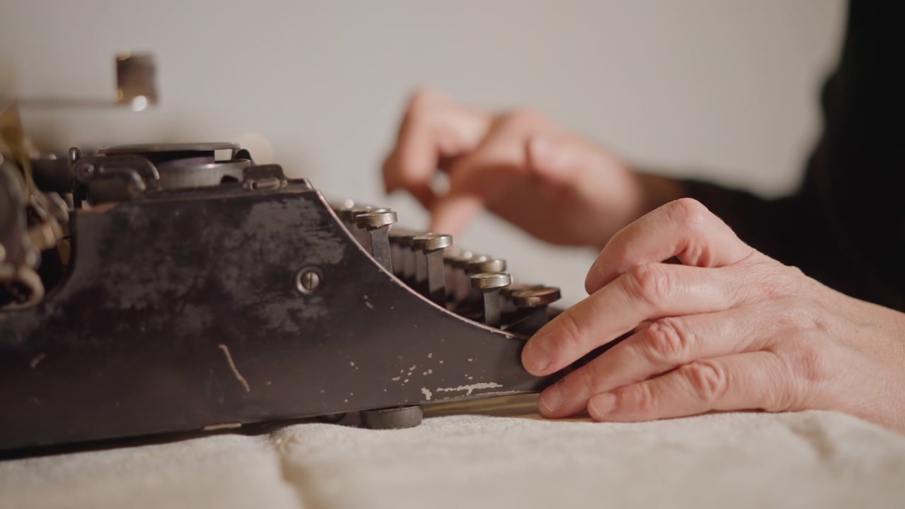 Closeup aged hands typing on typewriter, textured skin and steady fingers strike keys, slow cinematic motion with soft shadows, tactile sound of metal type and intimate portrait of experience