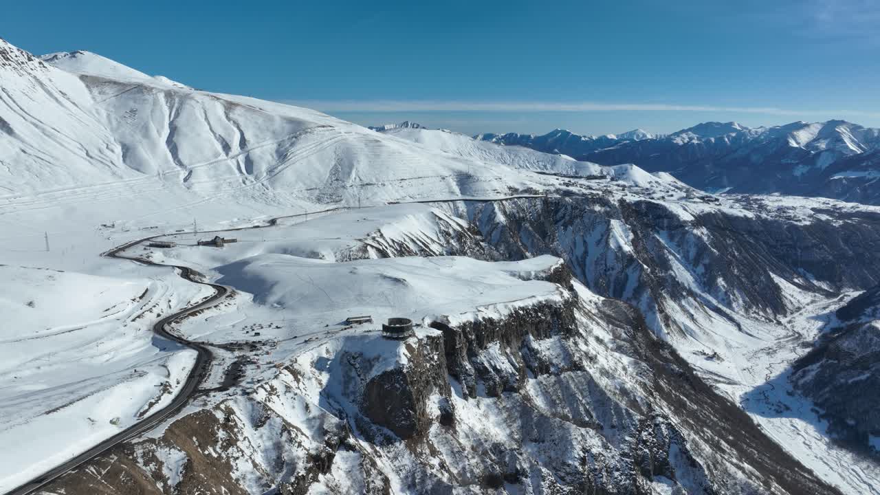 drone shot of A high-altitude road weaves through vast snow-covered plains, cutting a striking contrast against the untouched white terrain