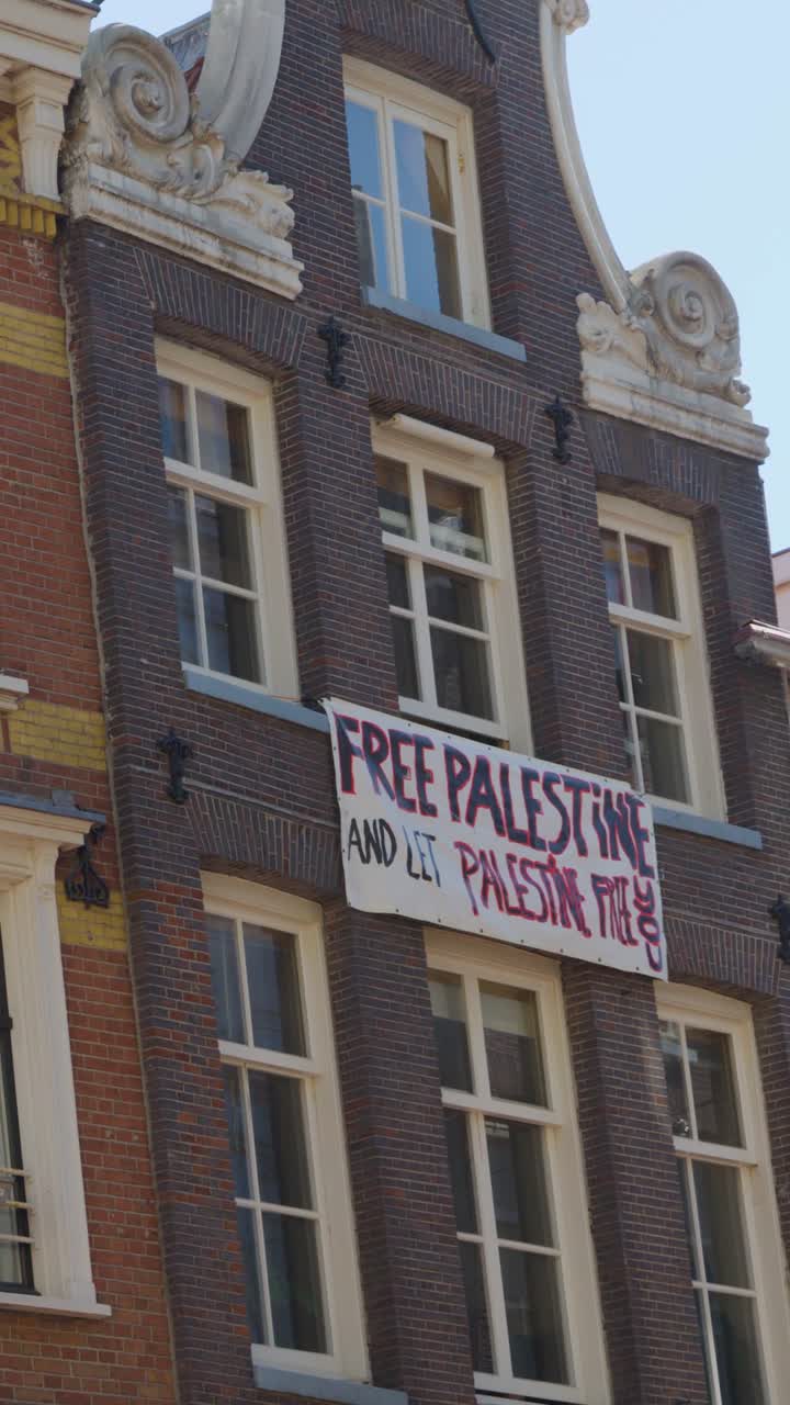Et protestbanner hænger fra en traditionel murstensbygningsfacade under en klar blå himmel.