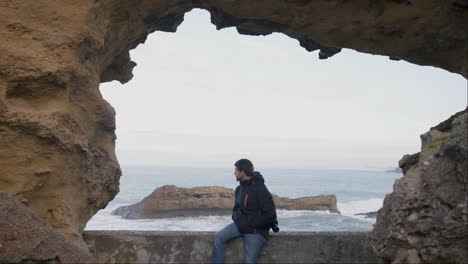 Young-sightseer-enjoys-a-lookout-inside-a-shallow-sea-cave,-Biarritz-France