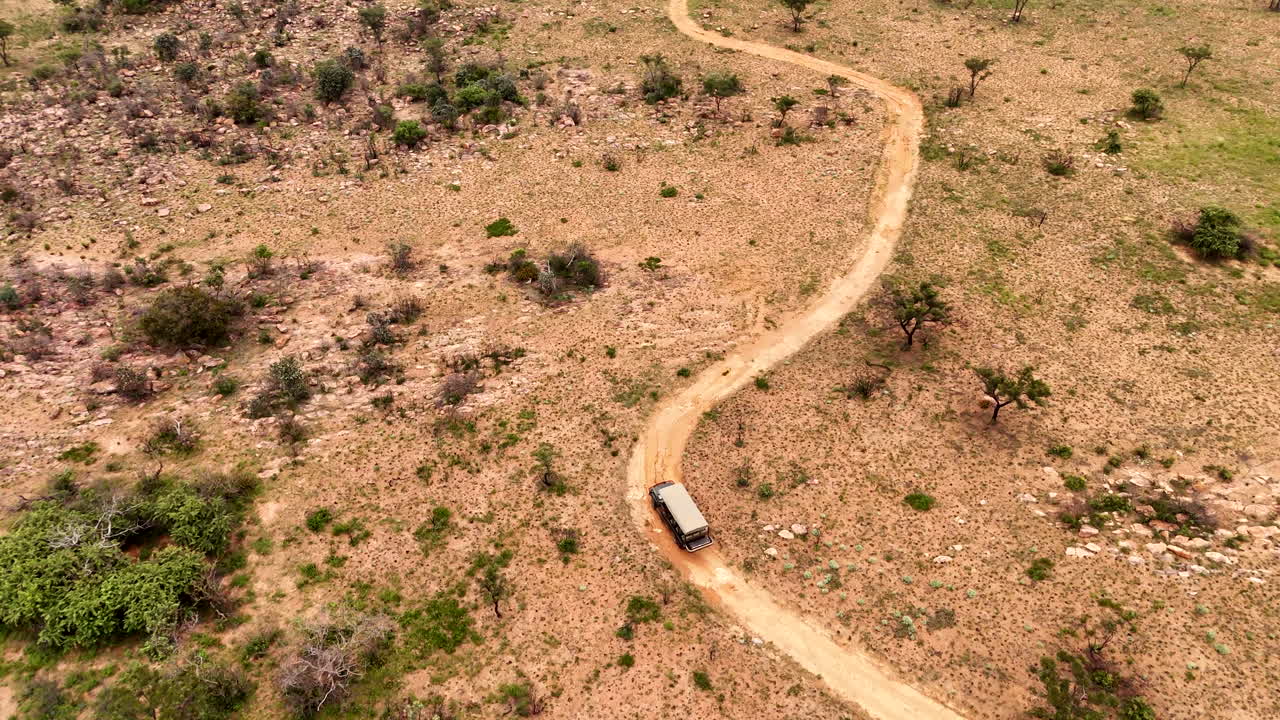 Safari game drive vehicle on African game reserve winding dirt road, aerial