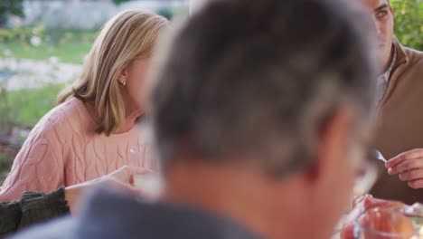 video of happy caucasian parents, daughter and grandparents eating at outdoor dinner table