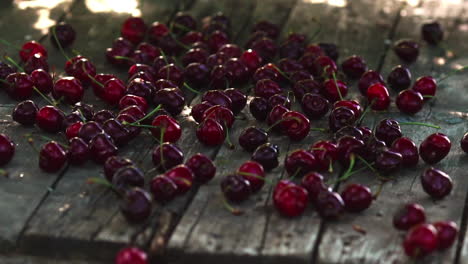 red berries of ripe cherries fall on a wooden table in slow motion