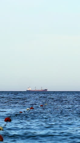 Blue sea water. Save swimming zone marked by buoys on sea. Ship sailing on the water far away. Vertical video