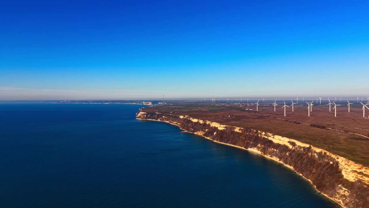 Fila di turbine illuminate dal sole sopra la costa di scogliere di gesso, Bulgaria. Vista elevata di torri bianche allineate lungo il bordo della scogliera con una scia di condensazione che solca il cielo sereno