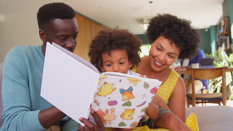 Multi-Generation-Family-With-Parents-Reading-Book-To-Son-And-Grandparents-Helping-Granddaughter