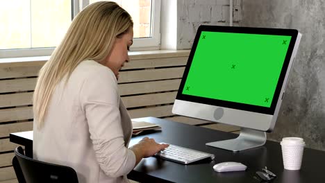 young female receptionist talking on phone in office and looking in monitor of her computer. green screen mock-up display