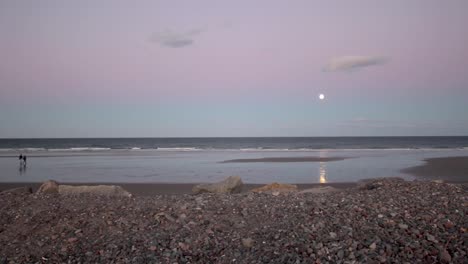 una pareja pasea por una playa de arena al salir la luna en una tarde de invierno en el noreste de estados unidos