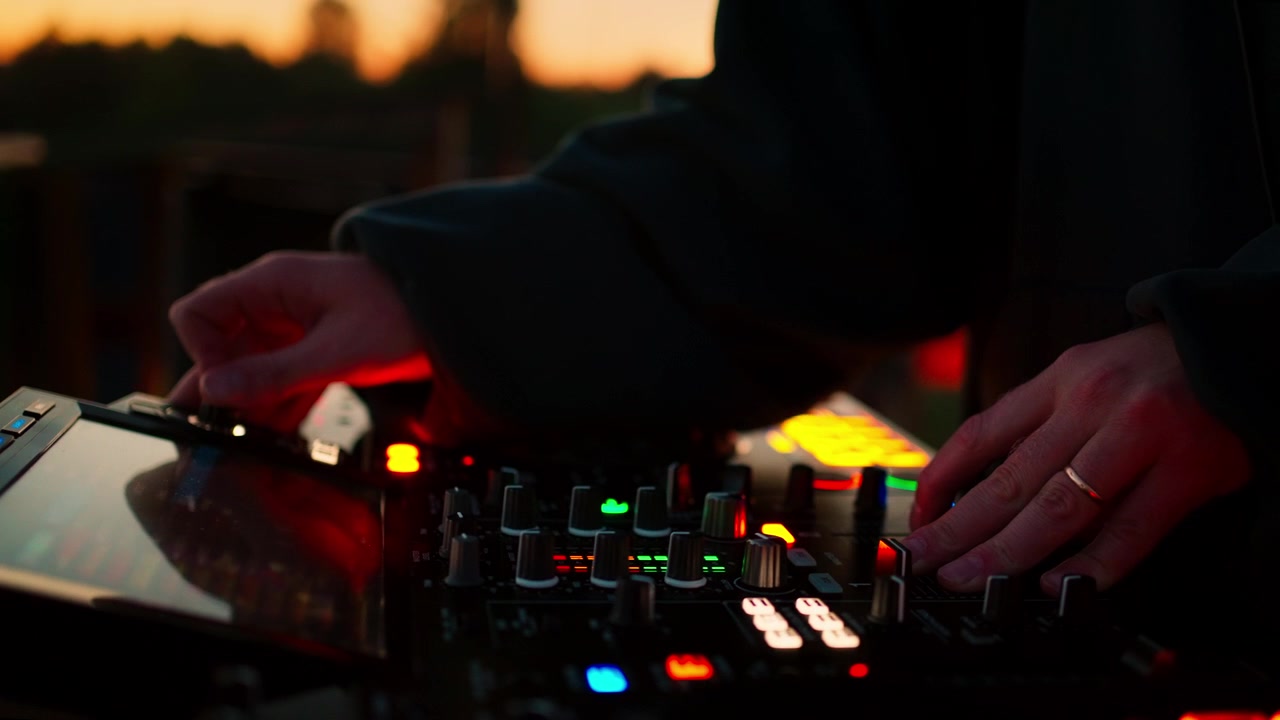 DJ's hænder justerer knapper på mixerpult ved solnedgang