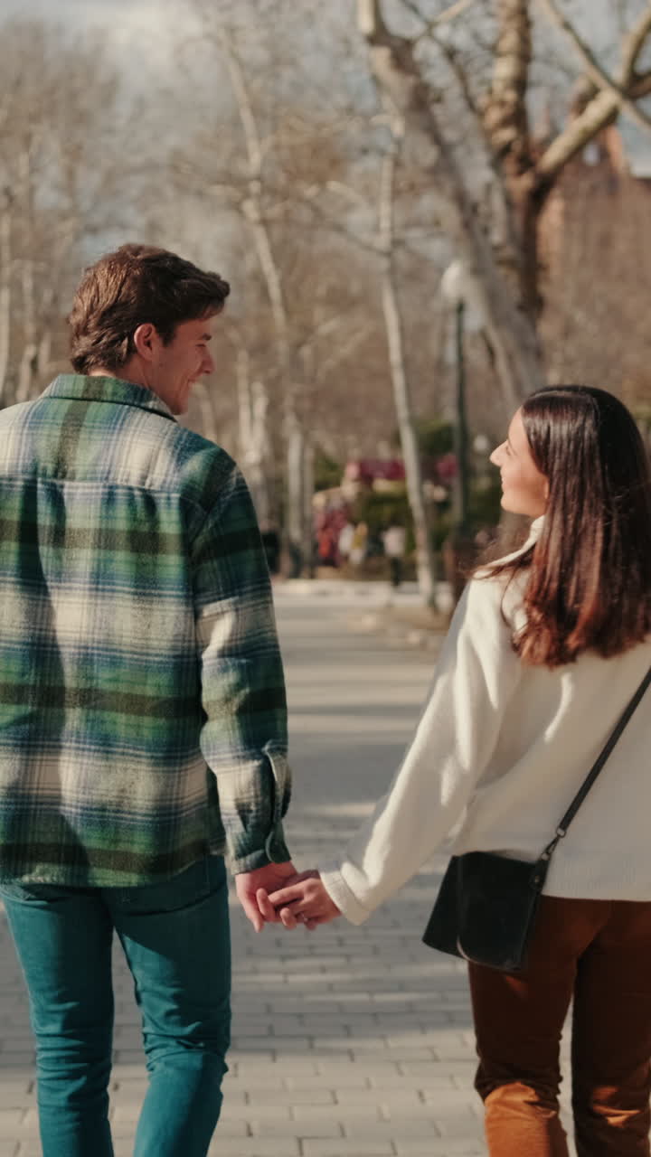 Joven pareja feliz caminando de la mano por la calle, vista posterior