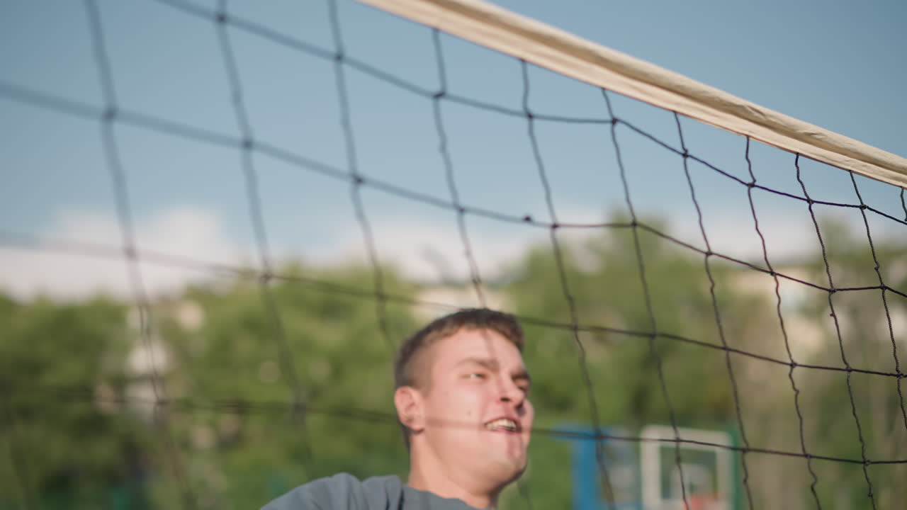 강렬한 훈련 중에 볼리볼을 다시 네트 위로 던지려고 하면서 높은 점프를 하는 남자. 배경에는 다양한 스포츠 시설과 나무가 포함되어 있습니다.