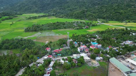 Toma-Aérea-De-Retroceso-De-La-Pintoresca-Ciudad-Rural-Filipina-Y-Torre-De-Comunicaciones-Con-Campos-De-Arroz-Y-Selvas-En-El-Fondo,-Virac,-Catanduanes,-Filipinas