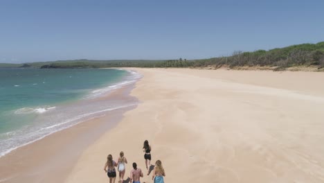 Jungs-Und-Mädchen-In-Badeanzügen-Laufen-In-Einer-Dreiecksformation-An-Einem-Strahlend-Blauen-Himmel-Und-Tosenden-Wellen-Den-Strand-Von-Papohaku-Auf-Maui,-Hawaii-Entlang