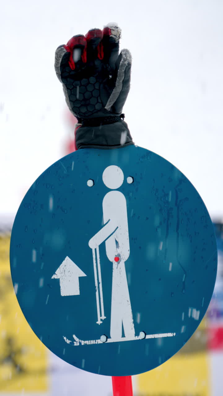 Close up of a ski sign with a ski glove on top in the snow with people skiing on the background. Vertical