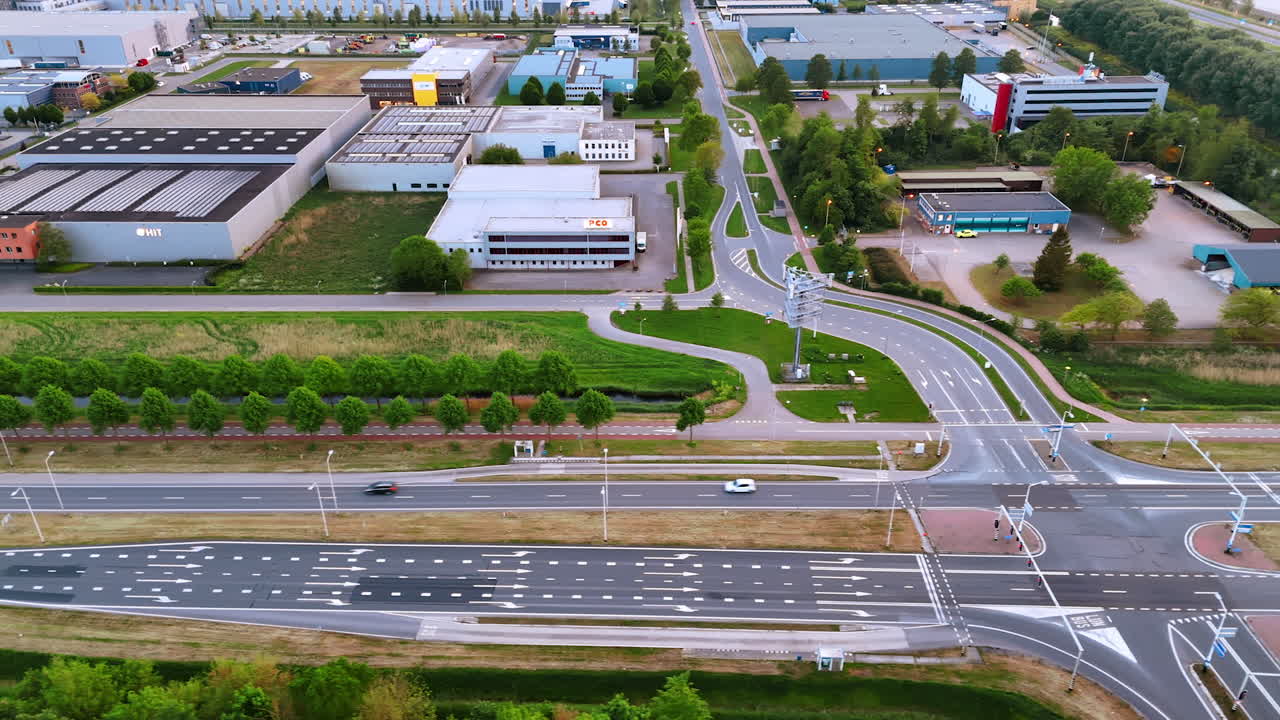 Flying along the road near industrial area. Low-rise large buildings among the green trees.