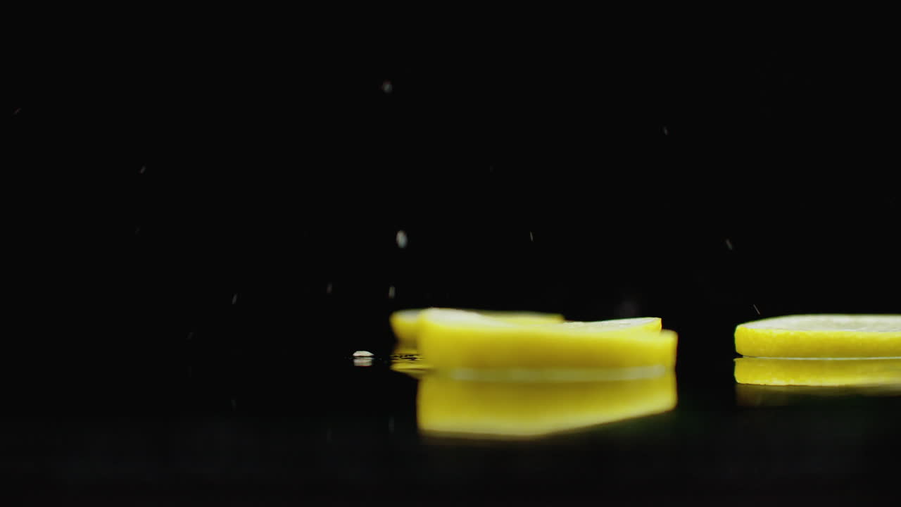 нарезанные лимонные кольца падают с брызгами воды на стакан на темном фоне. сочные цитрусовые фрукты.