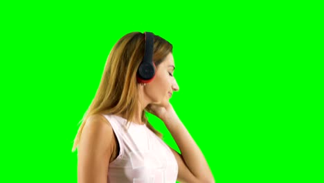 una hermosa rubia con auriculares disfruta escuchando música con fondo verde