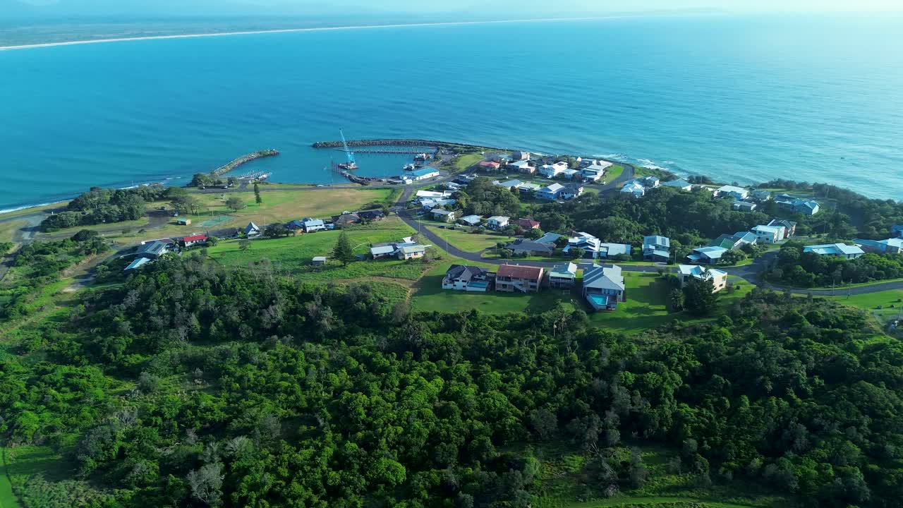 Drone aerial landscape of suburban town housing on residential street with bushland trees forest and boat harbour along headland ocean coastline at Crowdy Head Australia travel tourism infrastructure