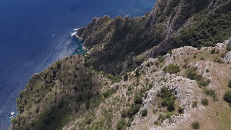 drone tilt reveal shot capturing the rugged capri mountain, surrounding rocks, and boats on the clear mediterranean waters