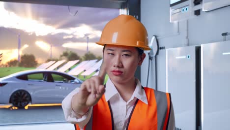 close up of asian female engineer with safety helmet disapproving with no index finger sign with home energy storage system in a modern garage