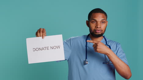 portrait of male nurse holding donate now sign, inviting people to contribute