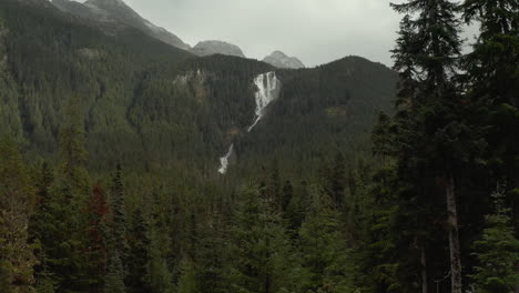 Drone-Revela-Una-Enorme-Cascada-Entre-El-Valle-De-La-Montaña-En-Un-Bosque-De-Pinos