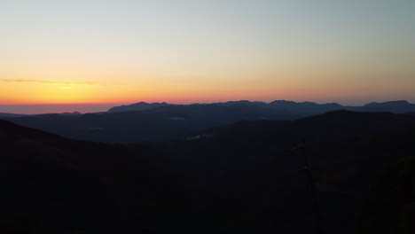 A-drone-pulls-back-of-the-sun-setting-over-the-horizon-of-mountain-ranges-near-Estepona,-Spain