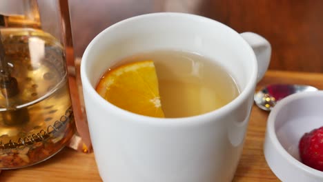 cerca de una taza de té con una rebanada de naranja, una tetera de vidrio y fresas