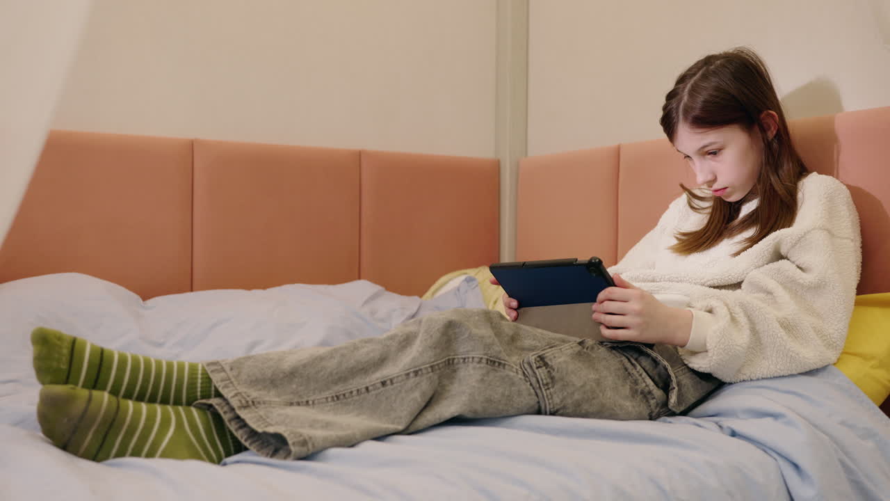 침대에 태블릿을 사용하는 십대 소녀