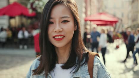 Retrato-De-La-Feliz-Joven-Encantadora-Mujer-Sonriendo-Alegremente-Y-Mirando-La-Cámara-En-El-Centro-De-La-Ciudad-Mientras-Es-Turista