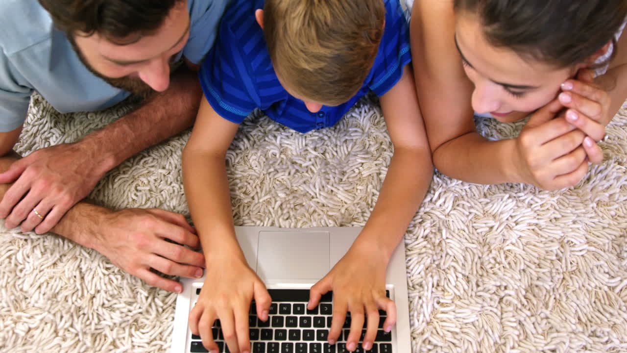 familia feliz mirando una computadora portátil tendida en una alfombra
