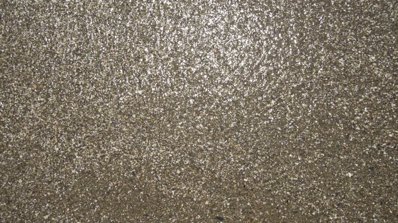 Gentle waves wash in and out across the grainy sand on the sunny beach.