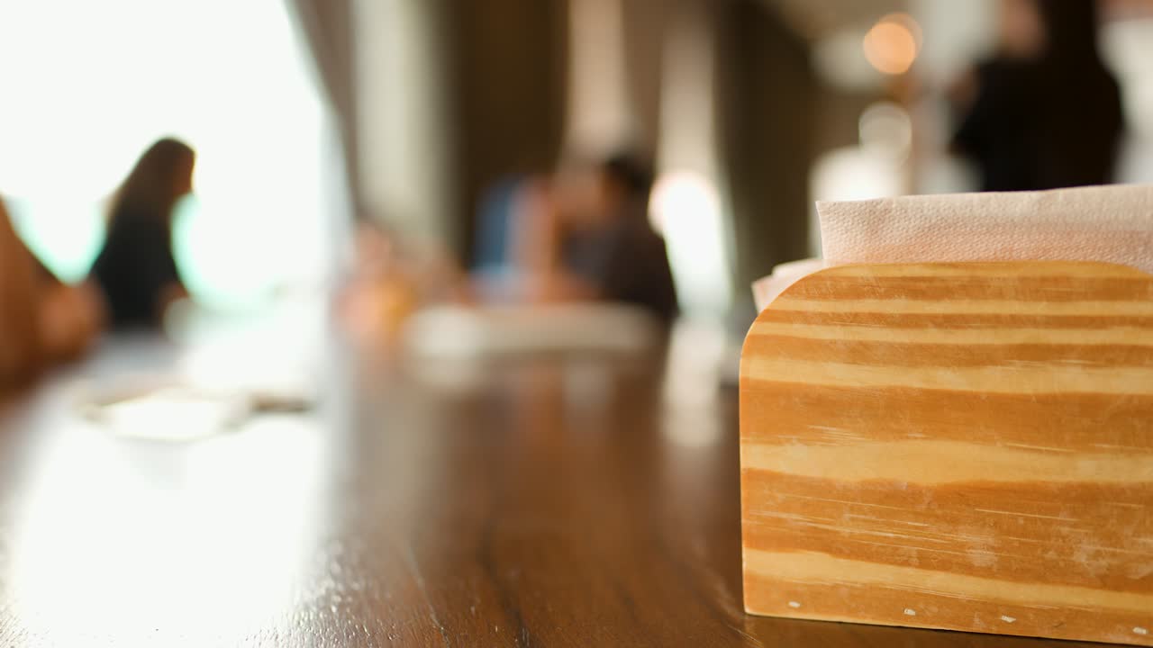 Close-up shot of a wooden napkin holder on a table with people dining in background