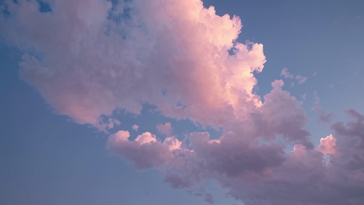 A serene video of pink-tinged clouds at sunset, captured from a low angle, highlighting the vastness