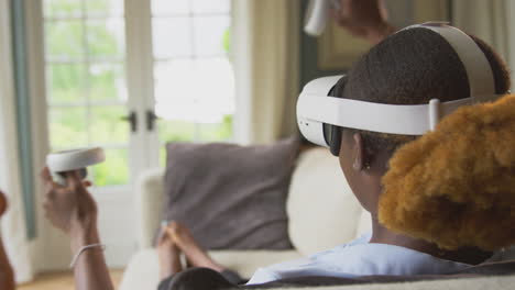 woman lying on sofa at home wearing vr headset with controllers and interacting with ar technology