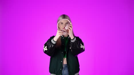 Junge-Blonde-Dame-Mit-Langen-Haaren-Hört-über-Kopfhörer-Musik-In-Urbaner-Kleidung,-Rosa-Chroma-Studiohintergrund,-Oberkörperaufnahme