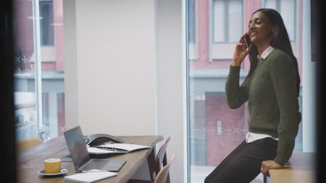 businesswoman sitting on desk in meeting room talking on mobile phone