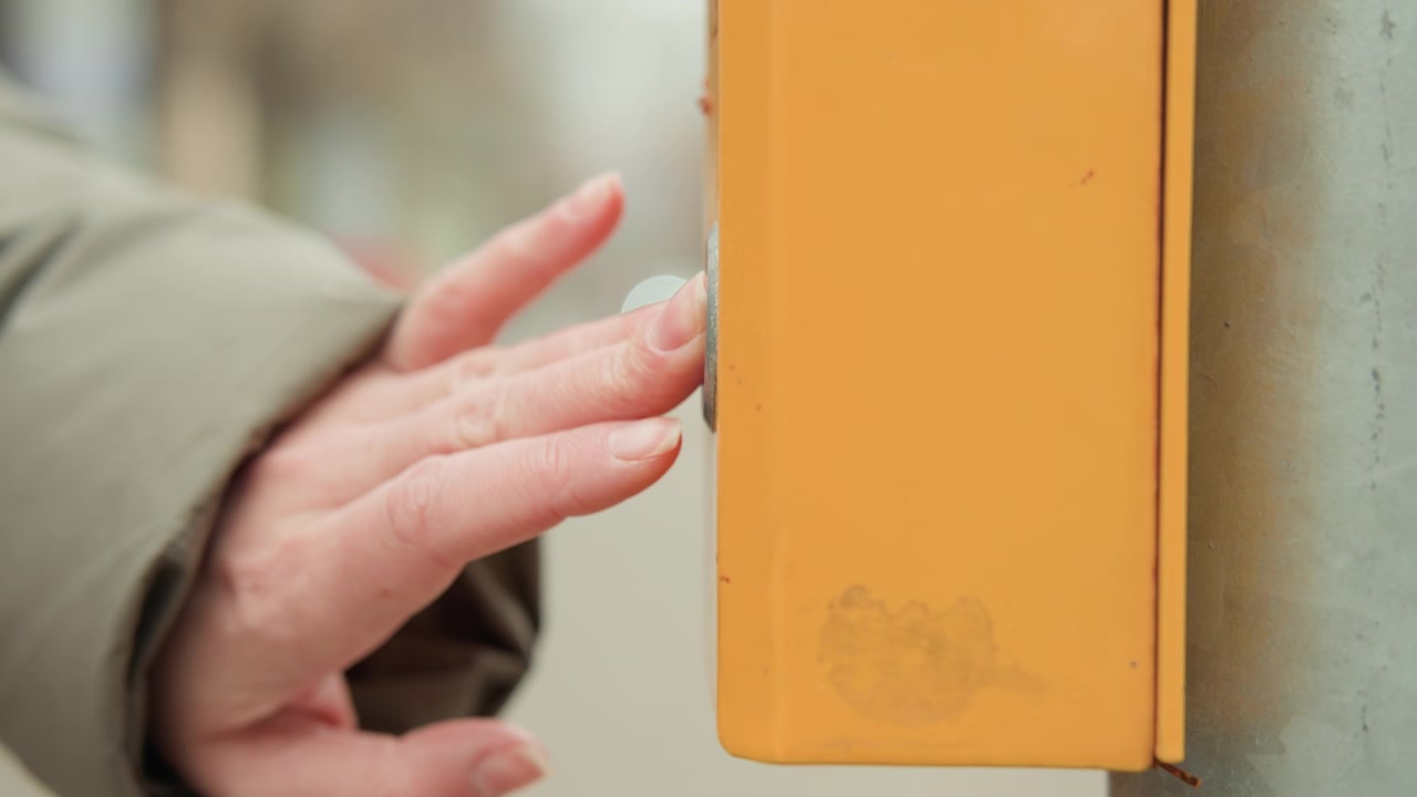Woman signals crossing. Pedestrian interacts with signal device. Closeup of woman touching crossing signal box. Urban scene captured as woman softly presses crosswalk button amid city lights