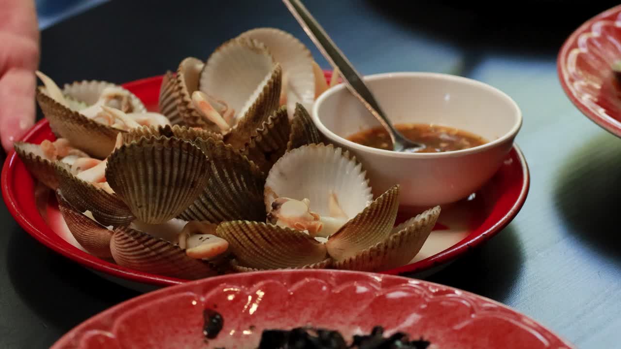 A vibrant seafood dish featuring clams and chili sauce on a red plate, captured in a lively dining setting
