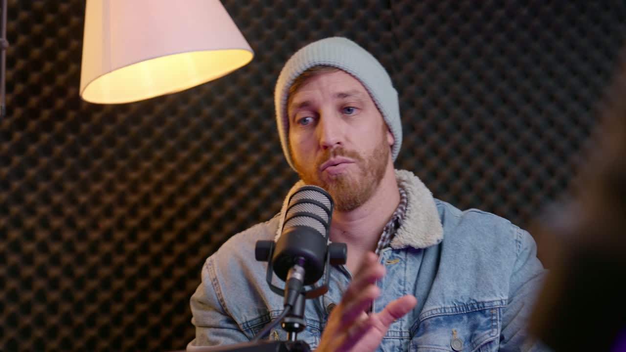 Podcaster or radio host finishing show, waving goodbye to viewers, removing headphones, relaxing back in their chair. Professional studio setup, post-show wrap-up, relief after a long session. tired