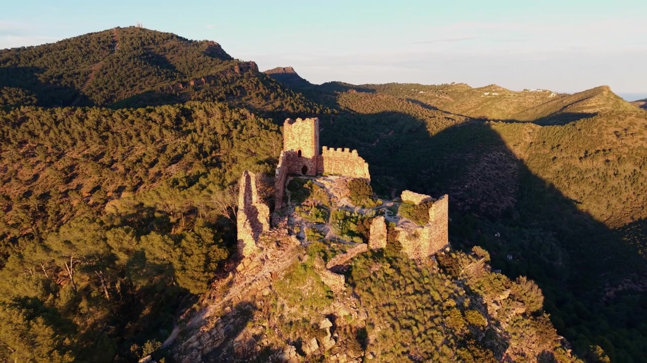 Rovine del castello medievale di Serra arroccate su una collina rocciosa al tramonto, circondate dalle montagne boscose del parco naturale della Sierra Calderona, Valencia, Spagna