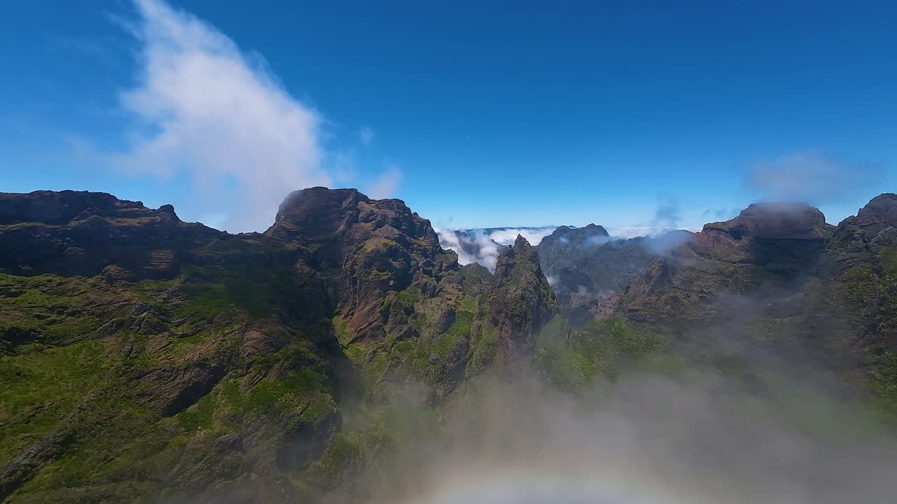 Wide aerial view of rugged mountain peaks and landscape of Madeira above the clouds. Drone view of island terrain and sky.