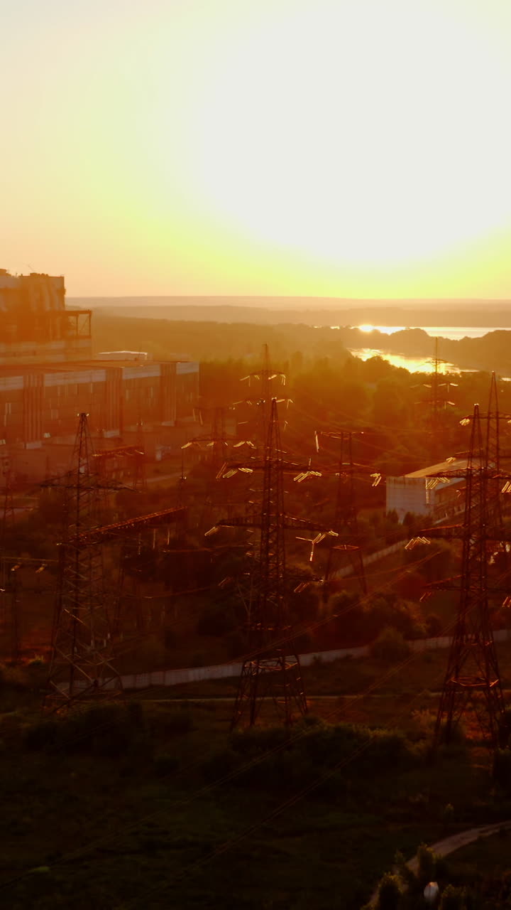 Industry in nature. High-voltage electric lines and industrial plant near the river at sunset. Pollution the environment. Vertical video