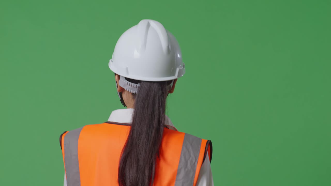 Close Up Back View Of Asian Female Engineer With Safety Helmet Looking Around While Walking In The Green Screen Background Studio