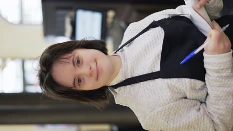 retrato de una mujer con síndrome de down inspeccionando estantes con mercancías en una tienda de comestibles usando un cuaderno