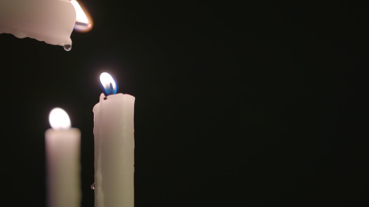 Una candela bianca che accende un'altra candela bianca con una candela accesa sullo sfondo al rallentatore.