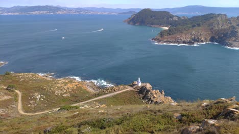 Vista-Elevada-Del-Camino-Al-Faro,-El-Mar-Y-La-Isla-Montañosa-Con-Playa-Y-Barcos-Navegando,-Día-Soleado,-Tiro-Panorámico-Girando-A-La-Derecha,-Islas-Cíes,-Pontevedra,-Galicia,-España