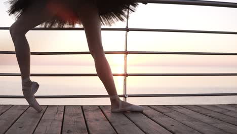 Close up of a beautiful ballerina&#039;s legs. A girl stretches her leg muscles, bending her feet. In pointe shoes. Morning on the seaside