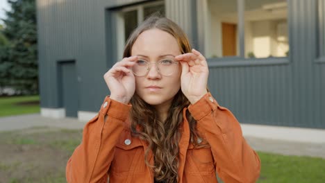 Young-Beautiful-Woman-Putting-On-Glasses-Smiling-Looking-Around-Facing-Camera-Close-Up-Medium-Shot-in-Casual-Clothing